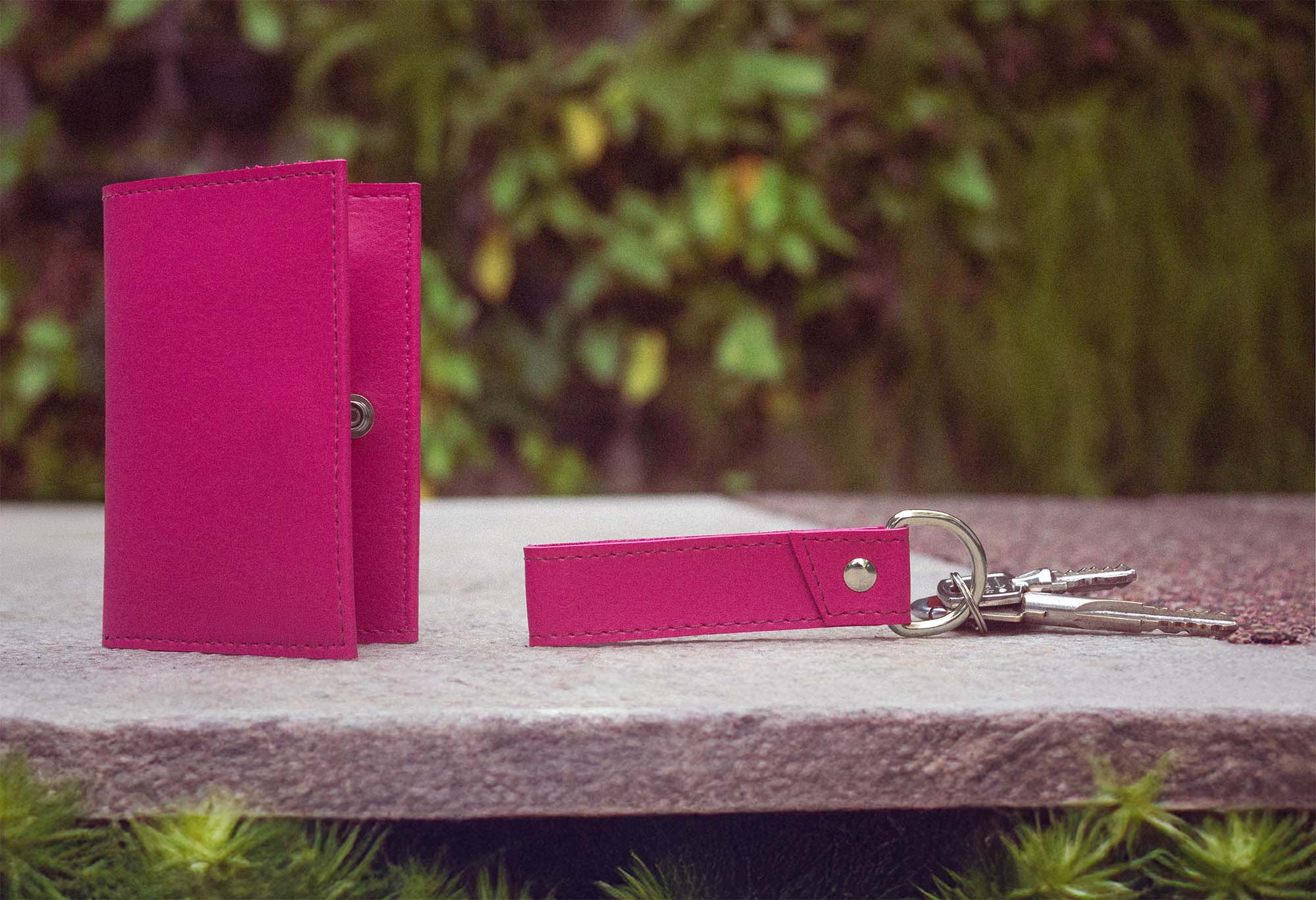 uma carteira e um chaveiro sobre um banco de pedra e planas ao fundo